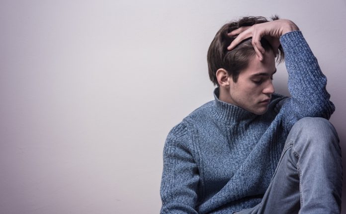 Depressed young man sitting in a corner by himself, feeling sad