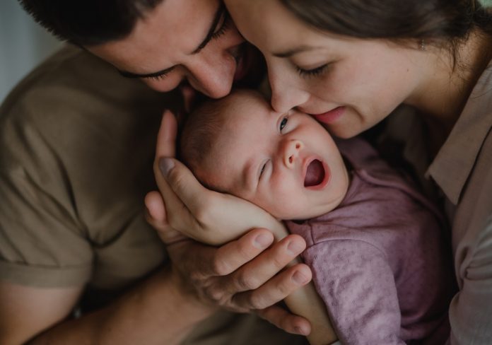 Close up of young parents holding and kissing their newborn baby indoors at home