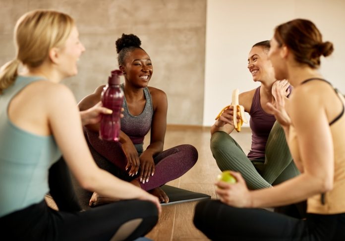 Happy black athletic woman having fun with her friends while taking a break from exercising in health club.